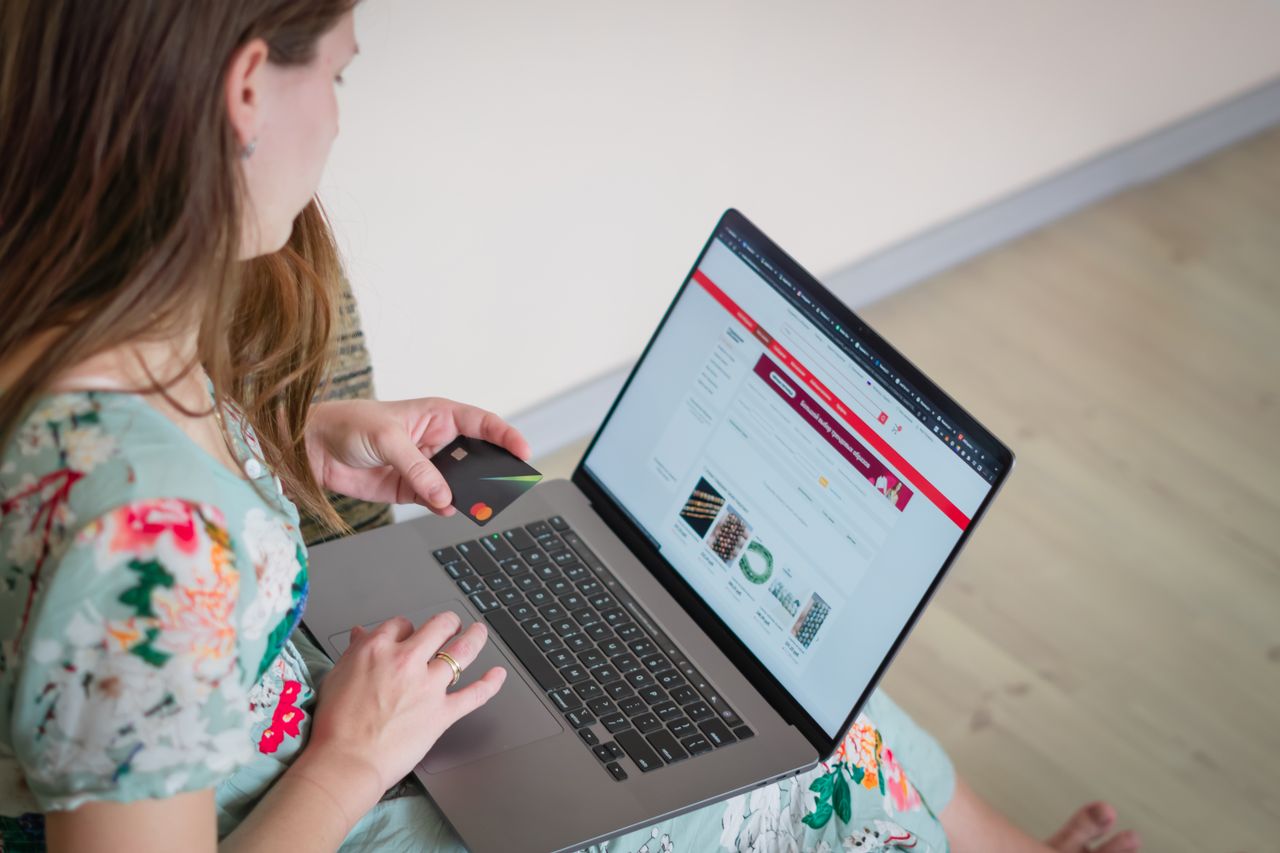 Home Woman in floral dress shopping online with a laptop and credit card indoors.