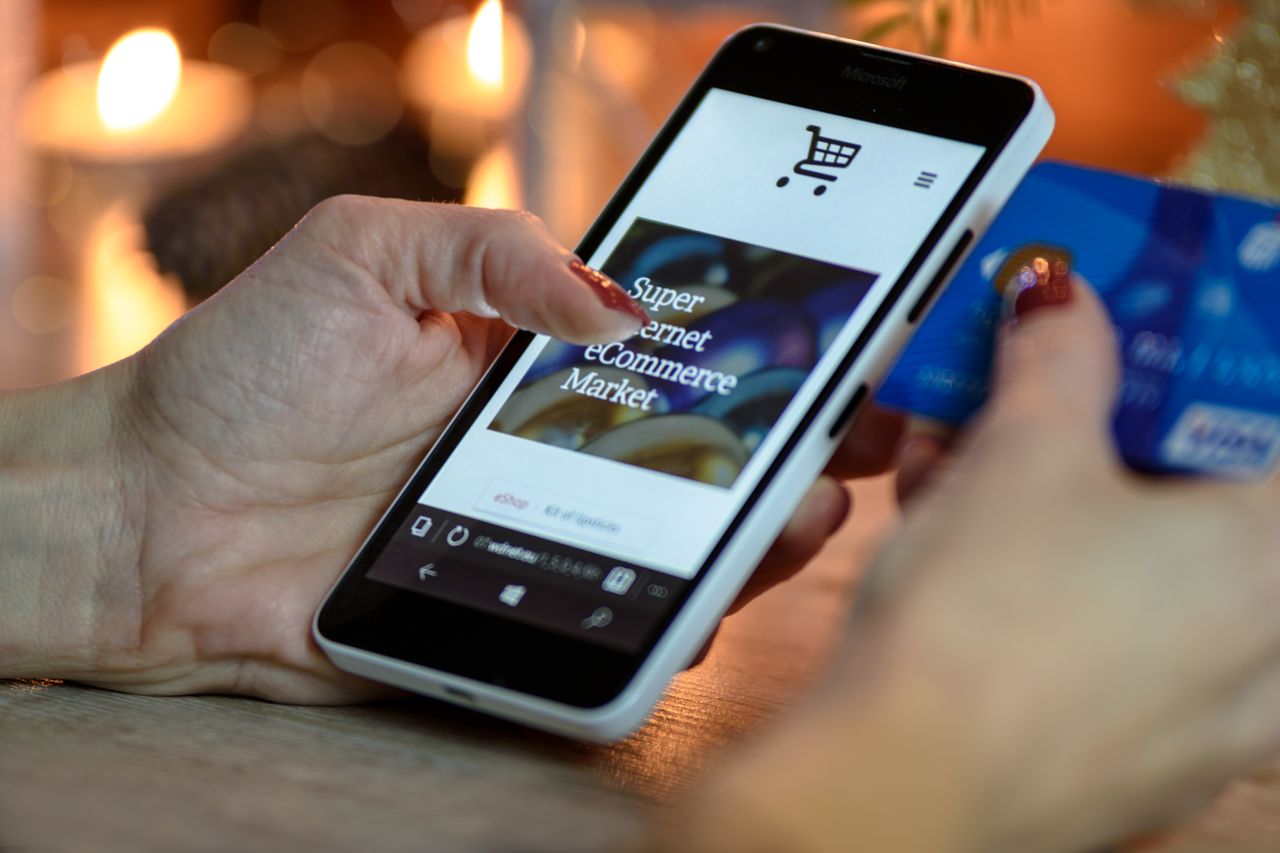 Home Woman using smartphone for online shopping with credit card in hand, festive background lighting.
