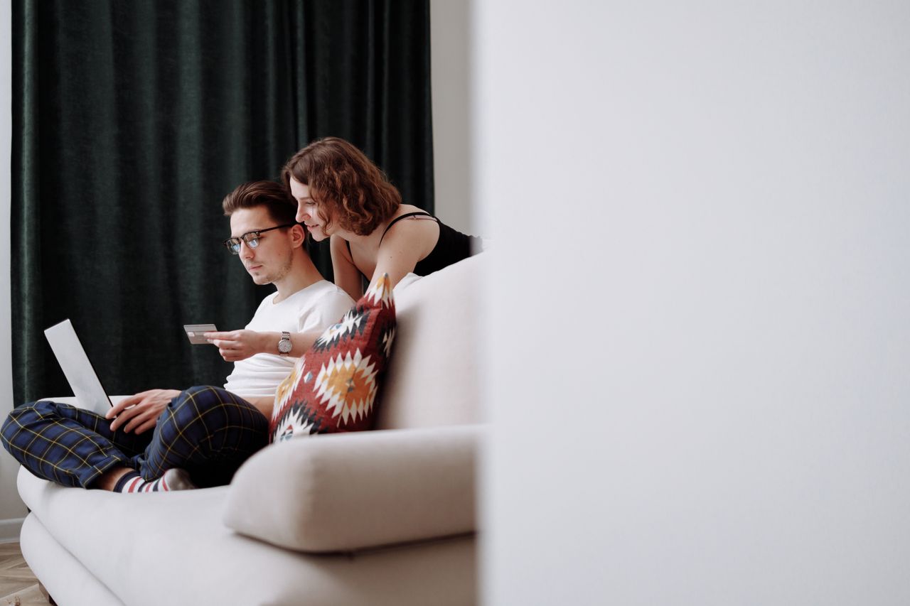 Home A couple sits comfortably on the couch while shopping online together.